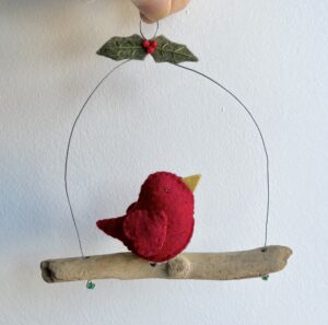 A single, small sized bird, handmade in red felt with a cotton holly print fabric chest. The bird is sat on a natural driftwood perch with a wire hanger that is decorated with  felt holly leaves and glass beads.

Approximate size 14cm width by 15cm height.