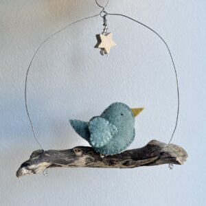 A single, small sized bird, handmade in duck egg green felt with a cotton mistletoe print fabric chest. The bird is sat on a natural driftwood perch with a wire hanger that is decorated with a wooden star and glass beads. Approximate size 14cm width x 15cm height.