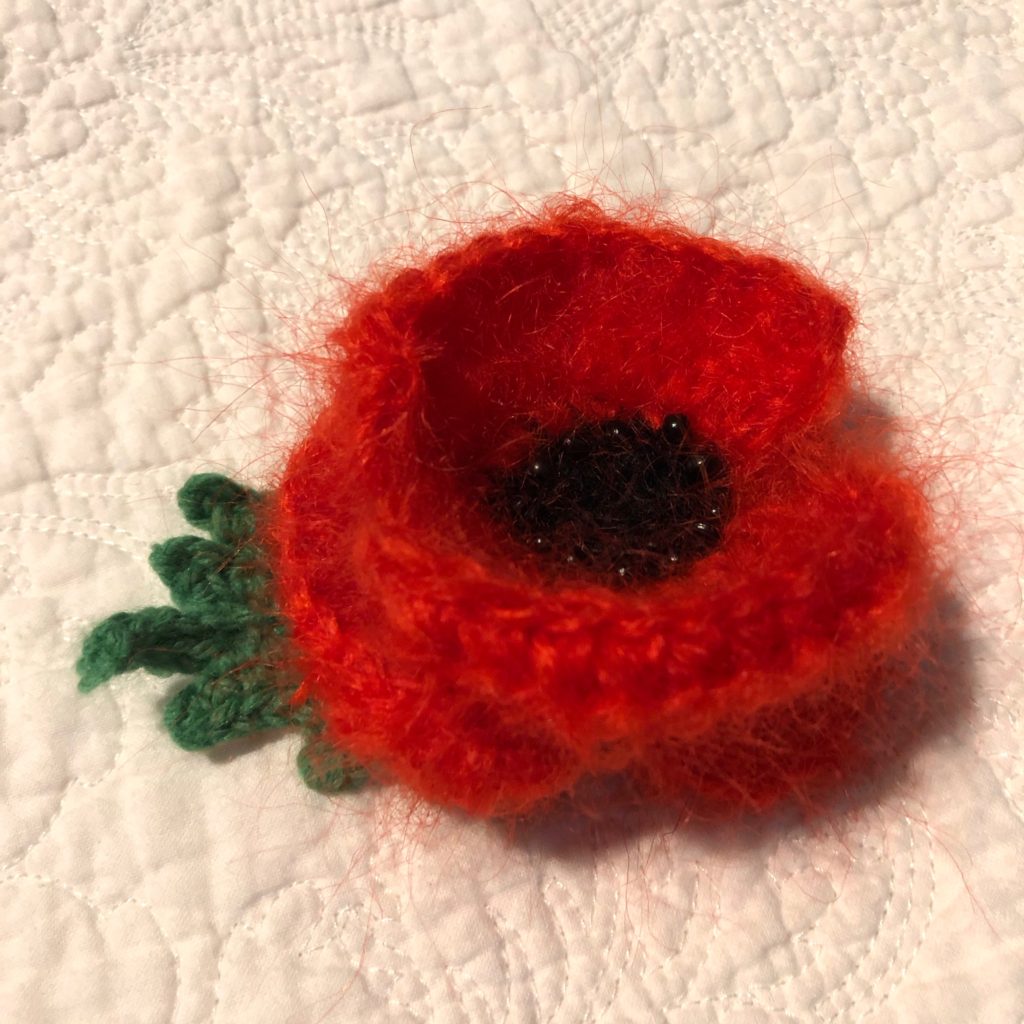 Crocheted Red Poppy brooch with beaded centre detail and green leaf.