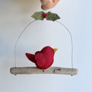 A single, small sized bird, handmade in red felt with a cotton holly print fabric chest. The bird is sat on a natural driftwood perch with a wire hanger that is decorated with felt holly leaves and glass beads. Approximate size 13cm width by 13cm height.