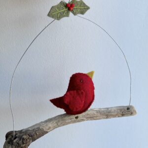 A single, small sized bird, handmade in red felt with a cotton holly print fabric chest. The bird is sat on a natural driftwood perch with a wire hanger that is decorated with felt holly leaves and glass beads. Approximate size 16cm width by 17cm height.