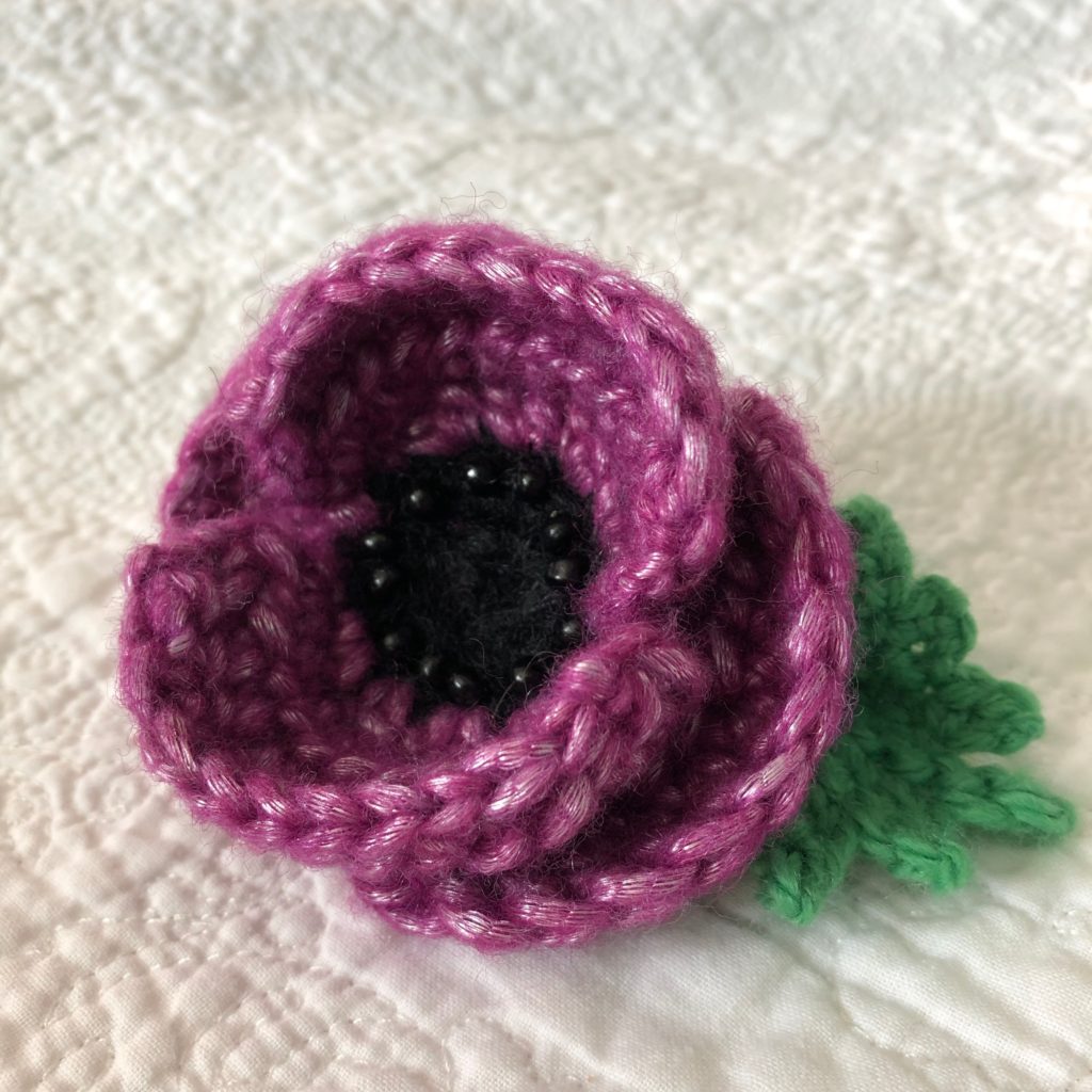 Crocheted Purple Poppy brooch with beaded centre detail and green leaf.