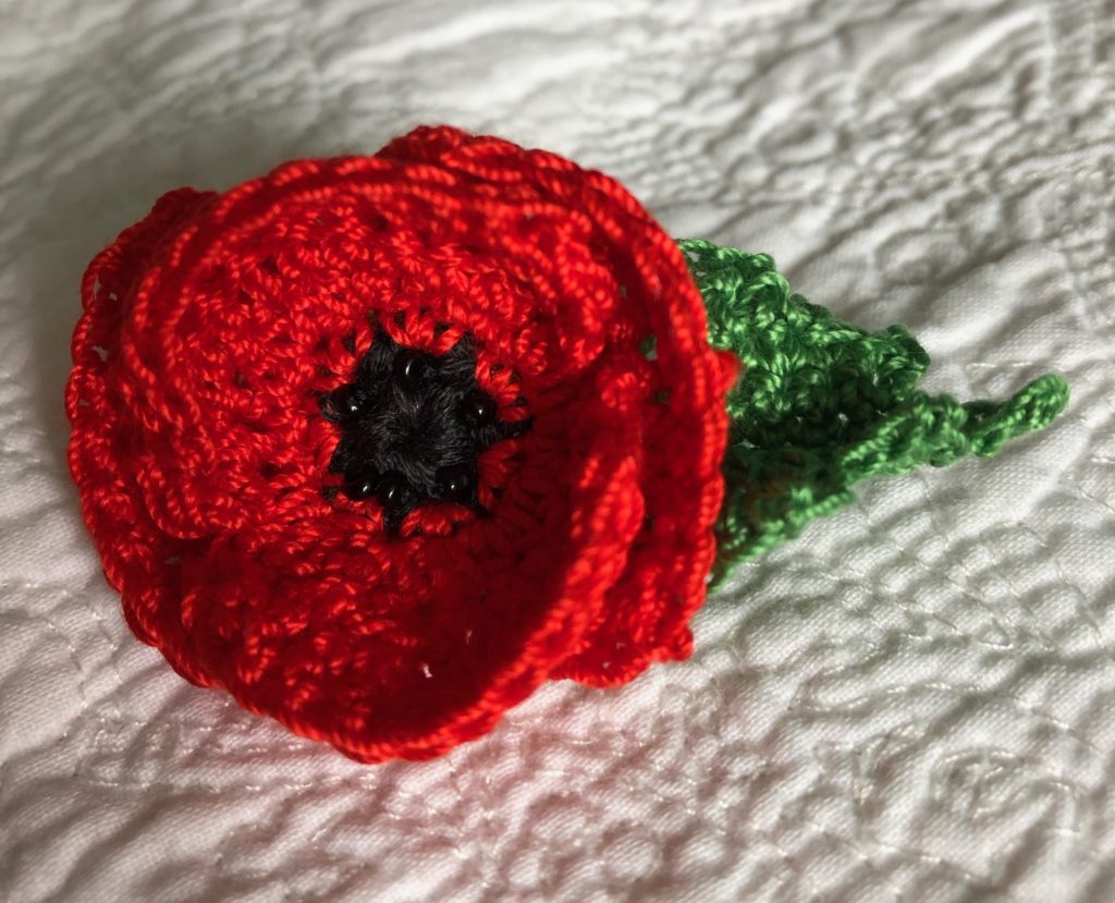 Small crocheted Red Poppy brooch with beaded centre detail and green leaf.