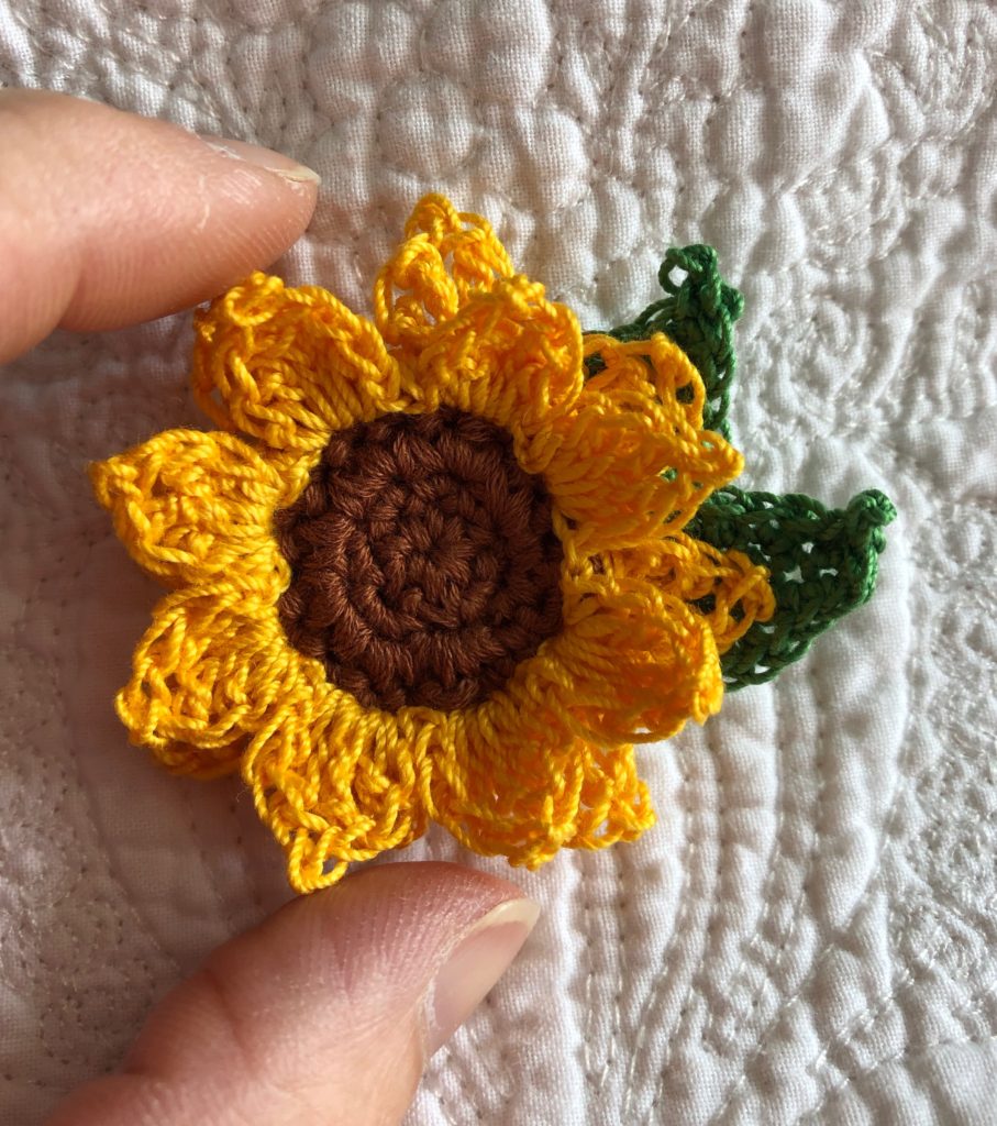 Small crocheted yellow Sunflower brooch with green leaves.