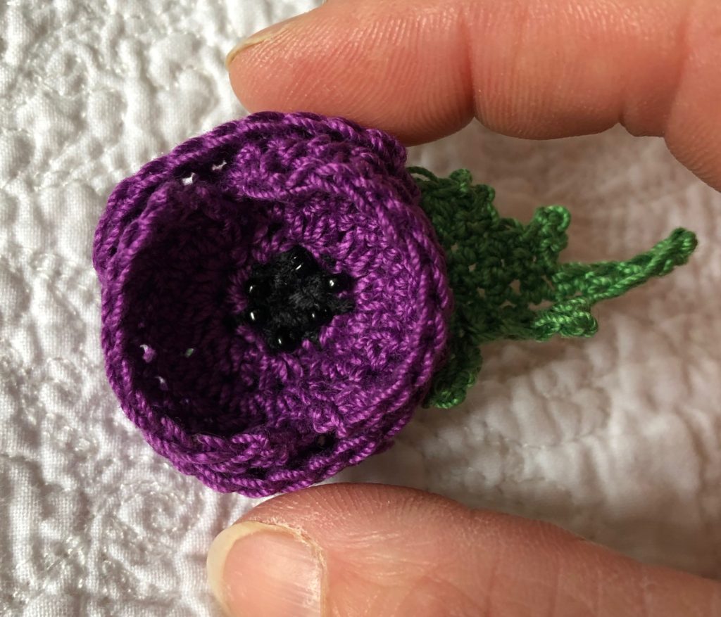 Small crocheted Purple Poppy brooch with beaded centre detail and green leaf.
