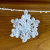 A hand crocheted garland of 10 snowflakes and glass beads, made in 100% white cotton. Approximate length 121cm.