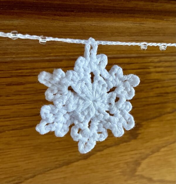 A hand crocheted garland of 10 snowflakes and glass beads, made in 100% white cotton. Approximate length 121cm.