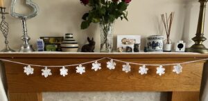 A hand crocheted garland of 10 snowflakes made using a white acrylic yarn with a shimmering thread running through. Approximate length 121cm.