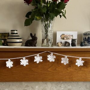 A hand crocheted garland of 10 snowflakes made using a white acrylic yarn with a shimmering thread running through. Approximate length 121cm.