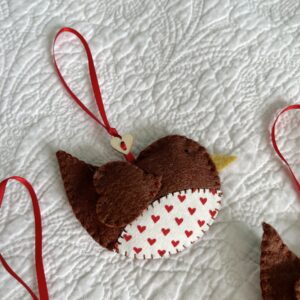 A hand cut and hand stitched, felt and fabric robin, with a red ribbon hanging loop and wooden button detail. Robins approximate size 8cm w x 5cm h. (excluding hanging ribbon.)