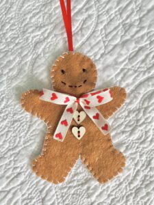 A hand-cut and handmade gingerbread man hanging decoration. Made in felt, with wooden buttons, glass beads,  and ribbon details.

Approximate size 11cm height (not including the hanging ribbon).