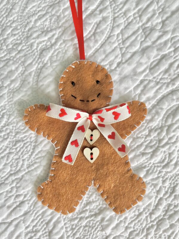 A hand-cut and handmade gingerbread man hanging decoration. Made in felt, with wooden buttons, glass beads, and ribbon details. Approximate size 11cm height (not including the hanging ribbon).