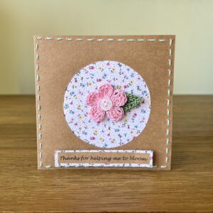 A single crocheted pink flower with button detail and a green leaf, with hand sewn boarder and Thanks for helping me to bloom message on the front. This card has a blank white paper insert for you to write your own message. Handmade, using 100% cotton.