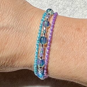 A set of three individual bracelets. A single stranded, elasticated bracelet made with glass beads in tones of blue, pastel purple and silver. One size. Elasticated, stretch fit. Two single stranded, glass beaded and 100% cotton bracelets. One in Lilac and one in Turquoise. Both fully adjustable.