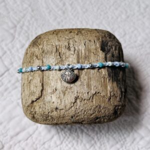 A handmade, crocheted, single stranded anklet (ankle bracelet). Made using glass beads in mint, light blue, silver and turquoise shades with a metal seashell charm and 100% cotton in a light blue colour with a fully adjustable sliding bead fastening.