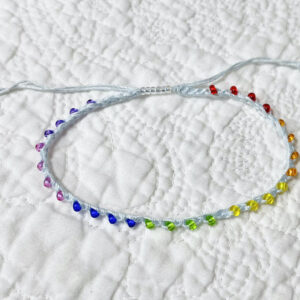 A handmade, crocheted, single stranded anklet (ankle bracelet). Made using glass beads in bright rainbow shades and 100% cotton in a light blue colour with a fully adjustable sliding bead fastening.