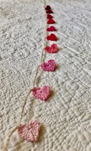 A crocheted garland of tiny hearts in a gradient of pale pink through to burgundy red.