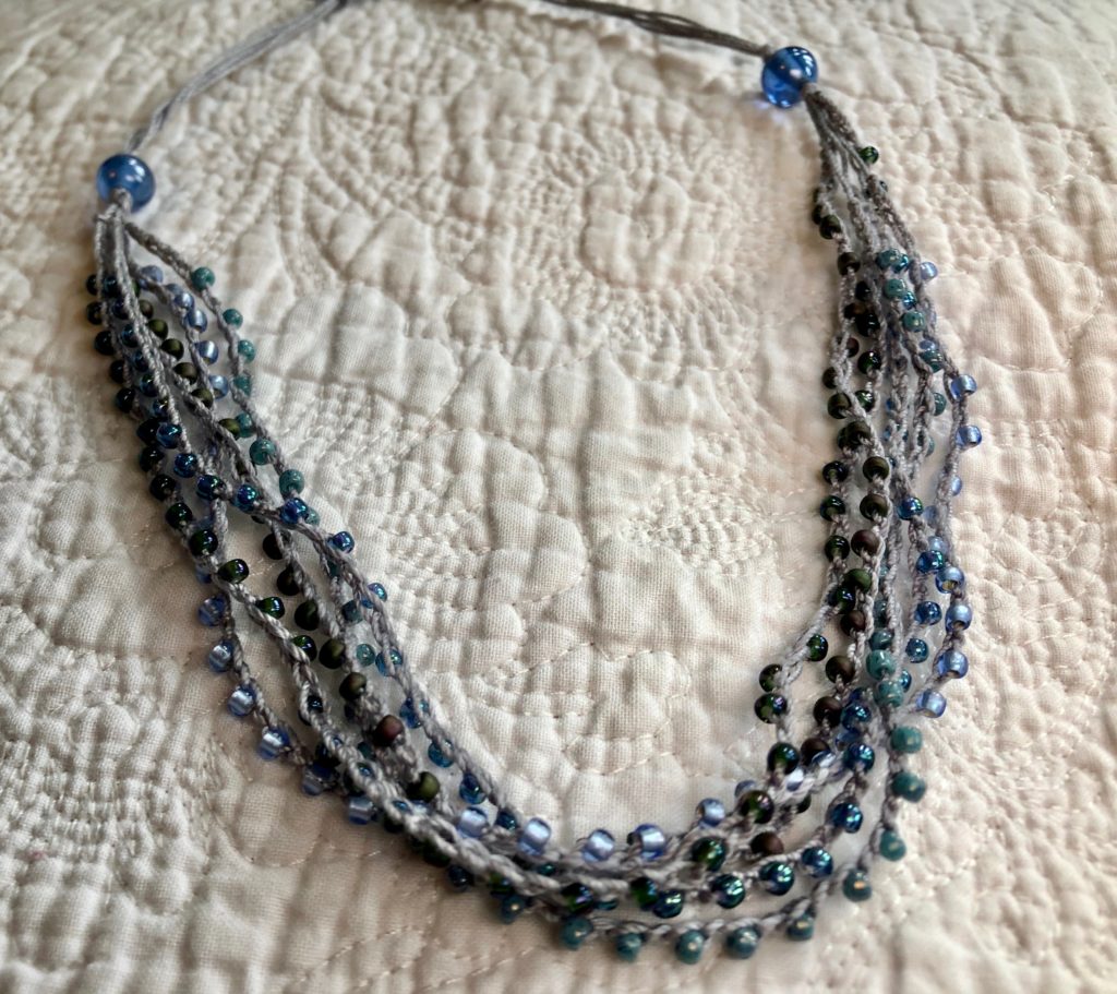 A multi stranded, grey crocheted cotton and glass seed bead necklace. Using tones of blue and grey glass beads.
