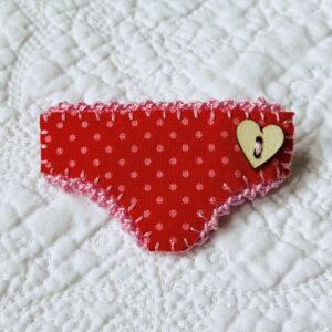 Handmade fabric and felt brooch with crocheted edging, a wooden heart button detail and a metal locking fastening. Approximate size 6cm Width x 4cm Height.