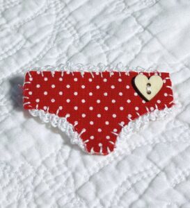 Handmade fabric and felt brooch with crocheted edging, a wooden heart button detail and a metal locking fastening. Approximate size 6cm Width x 4cm Height.