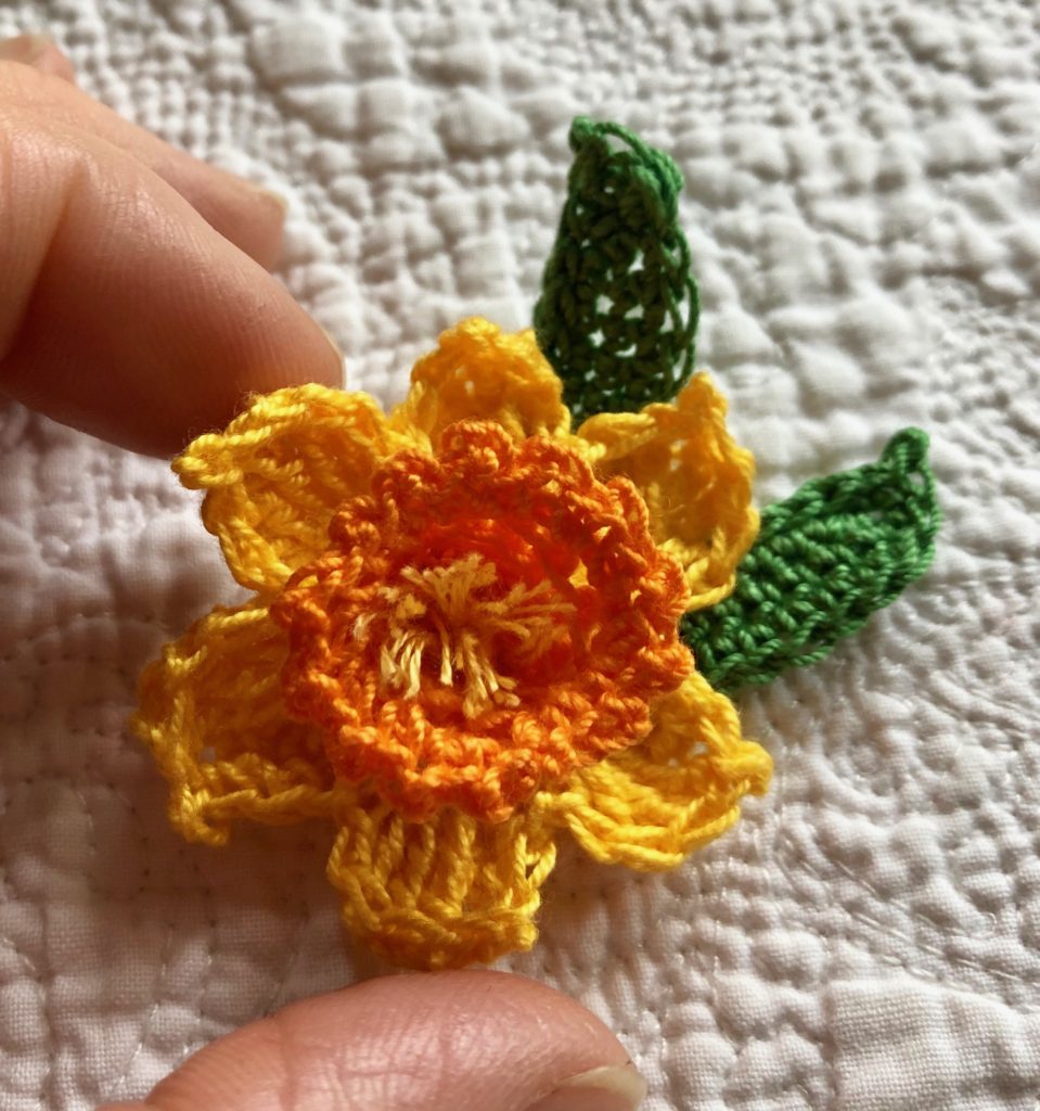 Crocheted daffodil brooch with green leaves.