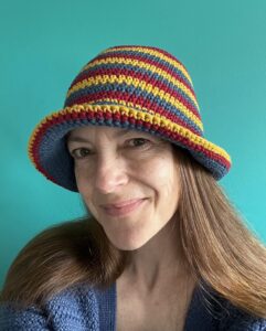 A hand crocheted bucket style hat, made using 100% cotton. It has multi coloured stripes in 3 bright colours, Denim Blue, Mustard yellow and Burgundy. One size.