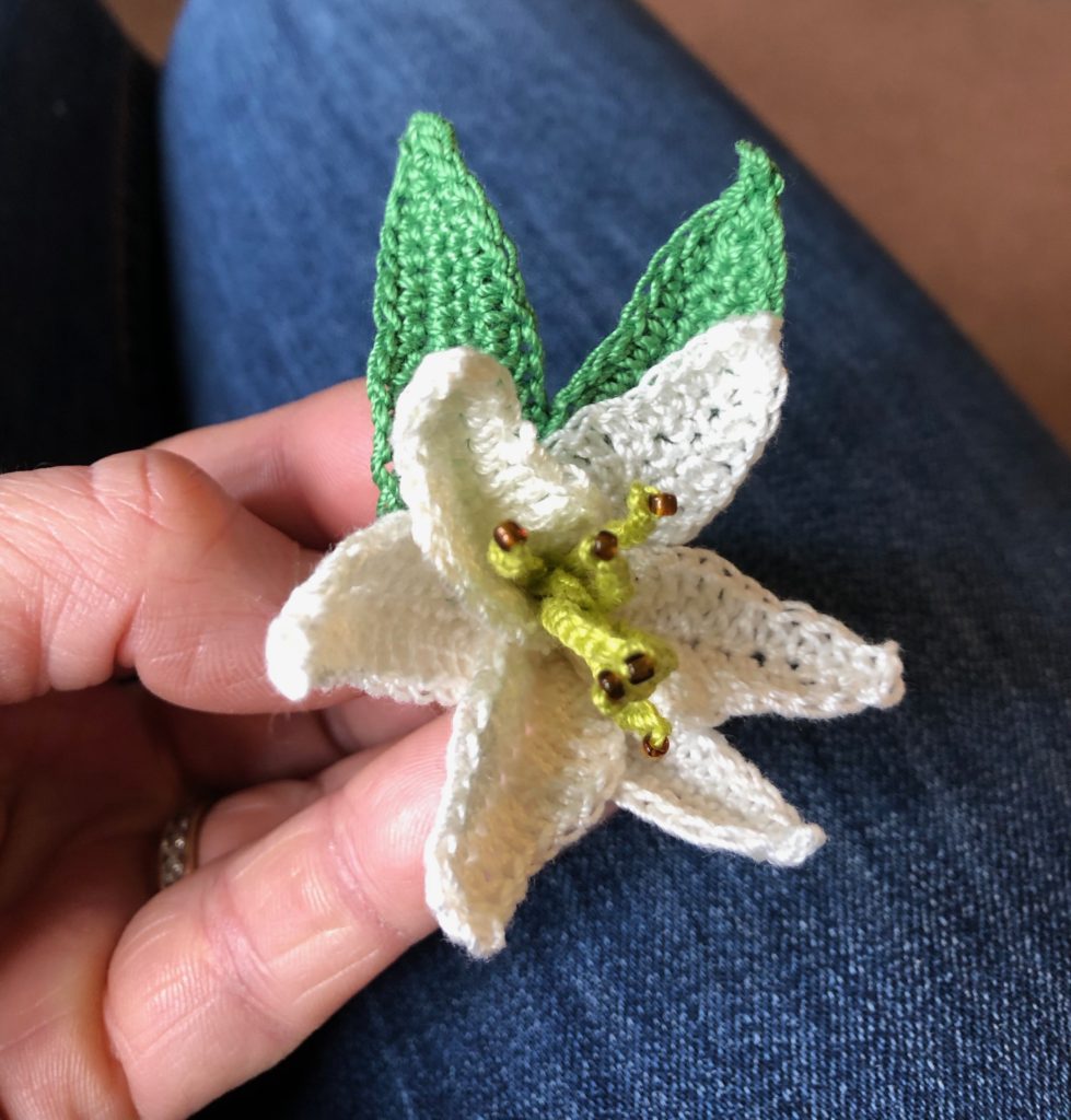 A white crocheted Lily with green leaves brooch.