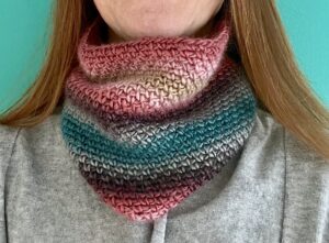 A handmade, close fitting, close textured, crocheted neck warmer, made using a soft and lightweight acrylic yarn in a mix of subtle pink and teal colours.