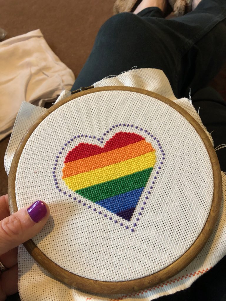 A cross stitched heart in striped rainbow colours with cross stitch detail boarder.