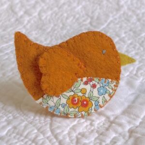 This little birdie brooch is completely hand cut, stitched, embroidered and embellished. It is made using a wool mix felt in rust orange colour with a floral patterned fabric chest. It has a metal locking fixing on the back.