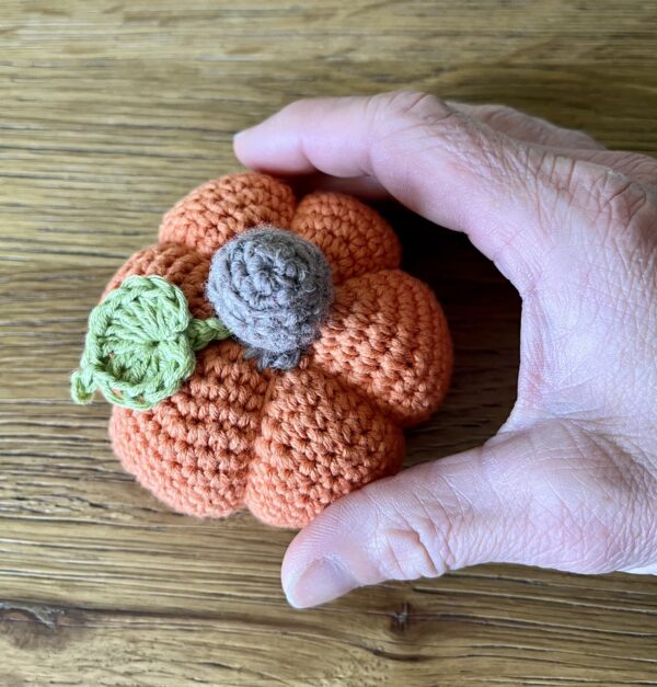 A small sized, handmade, crocheted pumpkin made in orange. With a brown stem and green leaf detail. Made using 100% cotton.