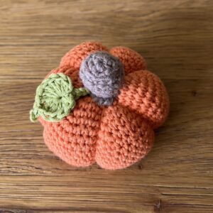 A small sized, handmade, crocheted pumpkin made in orange. With a brown stem and green leaf detail. Made using 100% cotton.