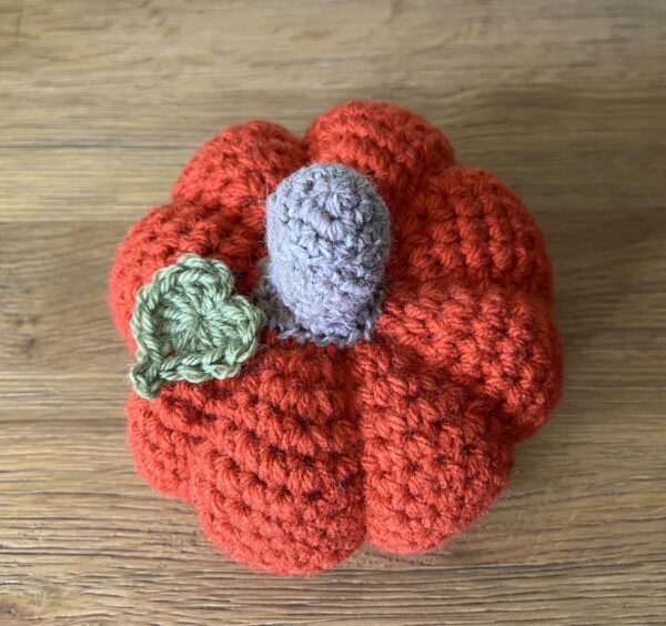 A large sized (8 section), handmade, crocheted pumpkin made in a spiced orange colour. With a brown stem and green leaf detail.