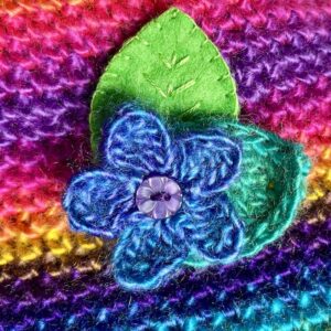 A single crocheted flower in a vibrant blue/purple mix colour, with vintage button detail and two leaf brooch. Flower made using 100% acrylic with one crocheted leaf and one hand stitched felt leaf. A locking metal brooch fastening on the back. Approximate size 6cm width x 6cm height.
