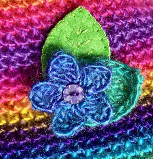 A single crocheted flower in a vibrant blue/purple mix colour, with vintage button detail and two leaf brooch. Flower made using 100% acrylic with one crocheted leaf and one hand stitched felt leaf. A locking metal brooch fastening on the back. Approximate size 6cm width x 6cm height.