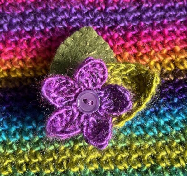 A single crocheted flower in a vibrant purple colour, with vintage button detail and two leaf brooch. Flower made using 100% acrylic with one crocheted leaf and one hand stitched felt leaf. A locking metal brooch fastening on the back. Approximate size 6cm width x 6cm height.