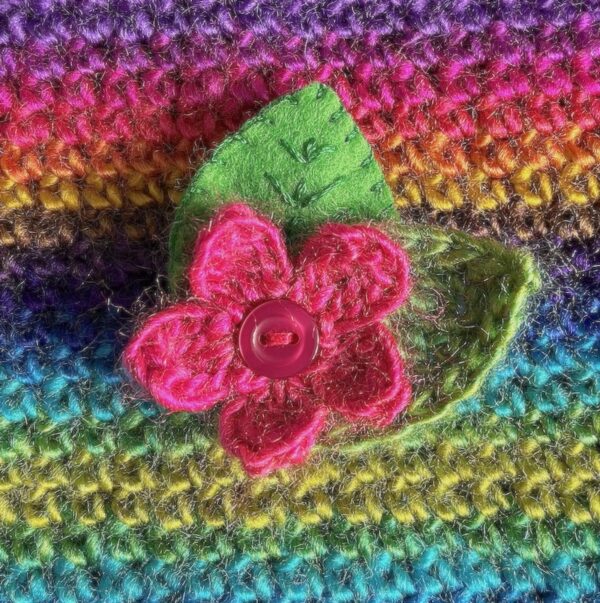 A single crocheted flower in a vibrant pink colour, with vintage button detail and two leaf brooch. Flower made using 100% acrylic with one crocheted leaf and one hand stitched felt leaf. A locking metal brooch fastening on the back. Approximate size 6cm width x 6cm height.