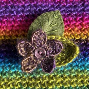 A single crocheted flower in a vibrant purple and gold mix colour, with vintage button detail and two leaf brooch. Flower made using 100% acrylic with one crocheted leaf and one hand stitched felt leaf. A locking metal brooch fastening on the back. Approximate size 6cm width x 6cm height.