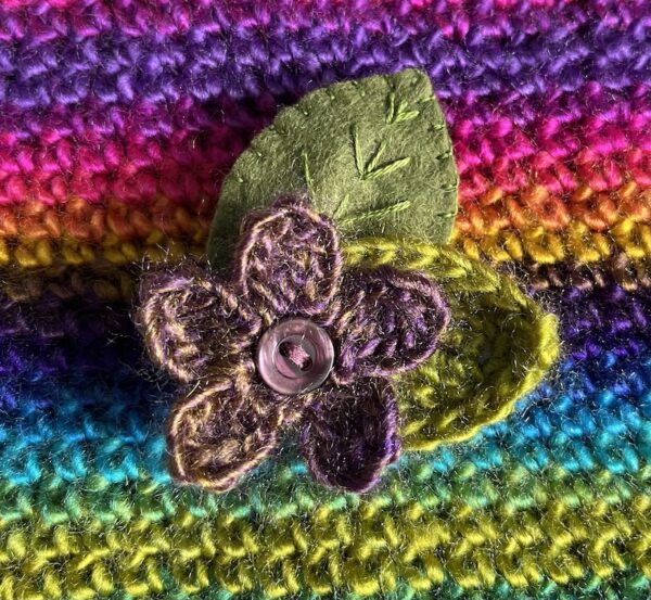 A single crocheted flower in a vibrant purple and gold mix colour, with vintage button detail and two leaf brooch. Flower made using 100% acrylic with one crocheted leaf and one hand stitched felt leaf. A locking metal brooch fastening on the back. Approximate size 6cm width x 6cm height.