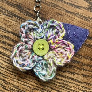 A hand crocheted multi-coloured flower and embroidered felt leaf with button detail keyring/bag charm.