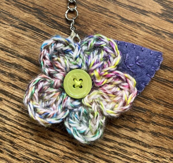 A hand crocheted multi-coloured flower and embroidered felt leaf with button detail keyring/bag charm.