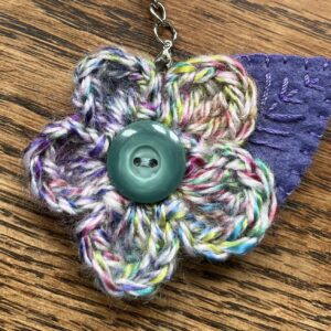 A hand crocheted multi-coloured flower and embroidered felt leaf with button detail keyring/bag charm.