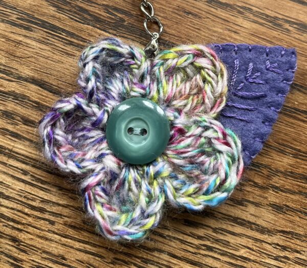 A hand crocheted multi-coloured flower and embroidered felt leaf with button detail keyring/bag charm.
