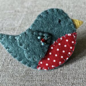 This little birdie brooch is completely hand cut, stitched, embroidered and embellished. It is made using a wool mix felt in a dark green colour with a spotty patterned fabric chest. It is hand embellished using glass beads and has a metal locking fixing on the back.