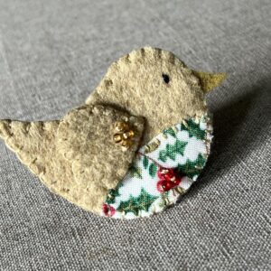 This little birdie brooch is completely hand cut, stitched, embroidered and embellished. It is made using a wool mix felt in a pale mustard colour with a holly patterned fabric chest. It is hand embellished using glass beads and has a metal locking fixing on the back.