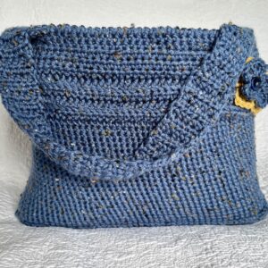 A handmade, crocheted shoulder bag with coordinating flower and leaf detail. Made in a denim blue, tweed style acrylic and wool mix yarn. Lined with a light blue heavy cotton fabric.