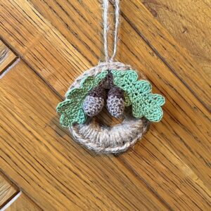 A handmade mini wreath hanging decoration. Crocheted in natural Jute and embellished with crocheted cotton oak leaves and acorns. Handmade using a wooden ring with 100% natural Jute, and 100% cotton embellishments. Approximate size of wreath 9cm height x 6.5cm width. Not including hanging loop.