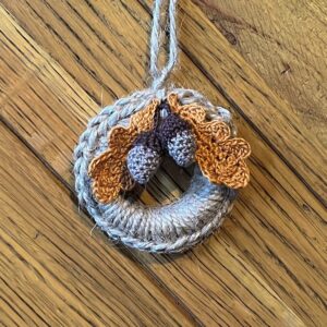 A handmade mini wreath hanging decoration. Crocheted in natural Jute and embellished with crocheted cotton oak leaves and acorns. Handmade using a wooden ring with 100% natural Jute, and 100% cotton embellishments. Approximate size of wreath 9cm height x 6.5cm width. Not including hanging loop.