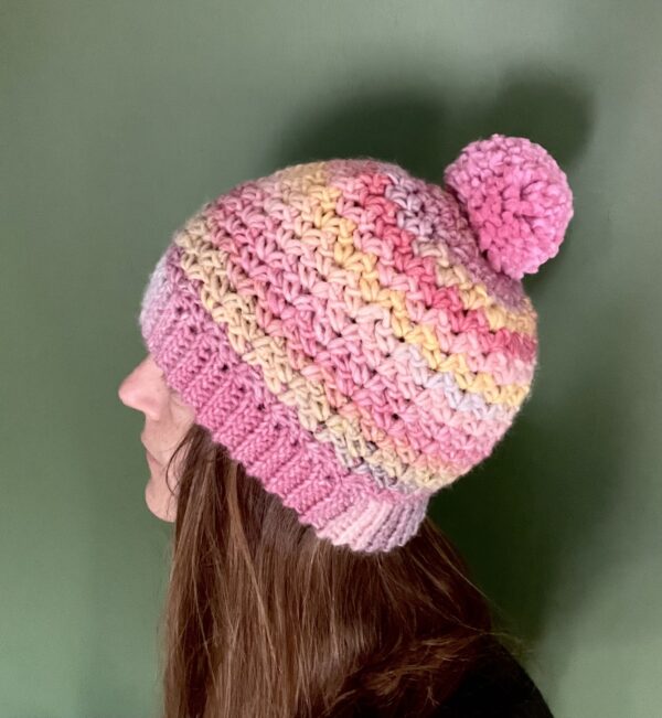 A soft and chunky textured hat with a large detachable bobble. Made in a subtle mix of pinks and yellows using a very soft and chunky, yet lightweight, 53% Wool/47% acrylic mix yarn. The bobble is made using a pink coloured 100% Acrylic yarn .