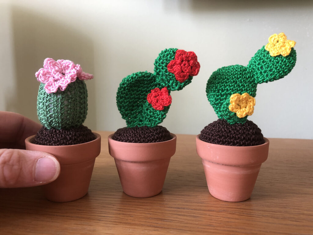Handmade, crocheted mini cactus plants in terracotta pots.